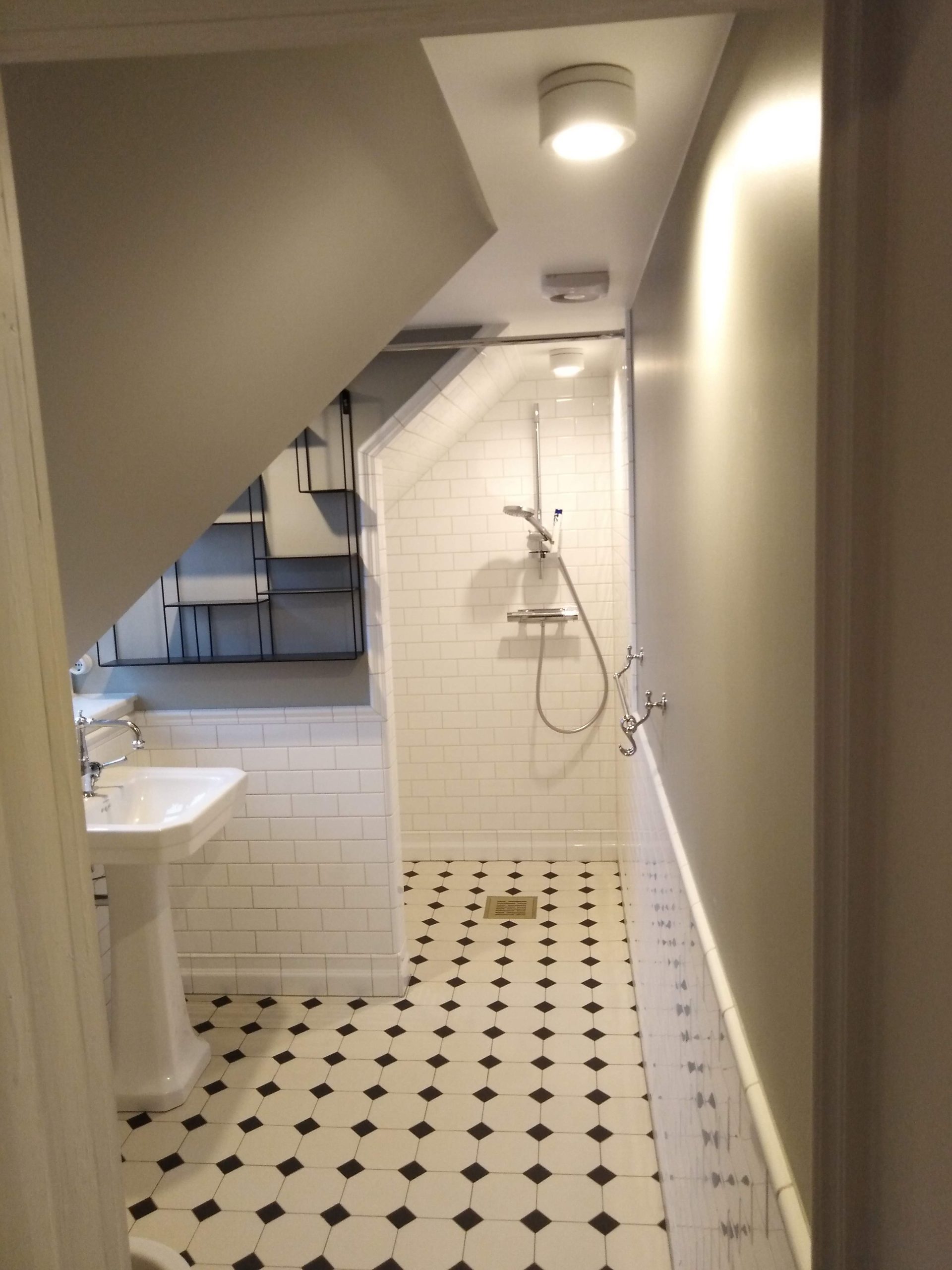 Badrumsrenovering av långsmalt badrum med klassiskt schackrutigt golv och ljusa väggar, skapar rymd.