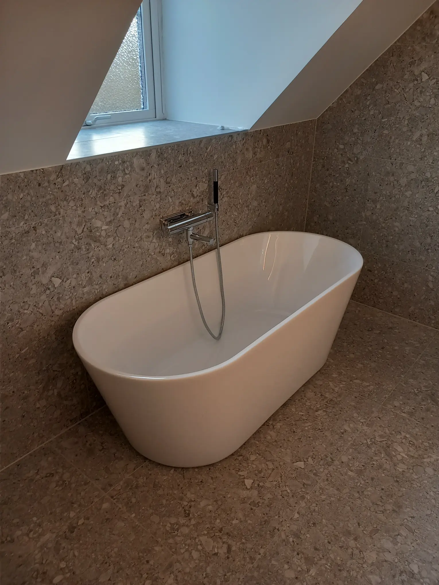 Badrumsrenovering med elegant fristående badkar under snedtak, skapar en lyxig och avkopplande atmosfär.