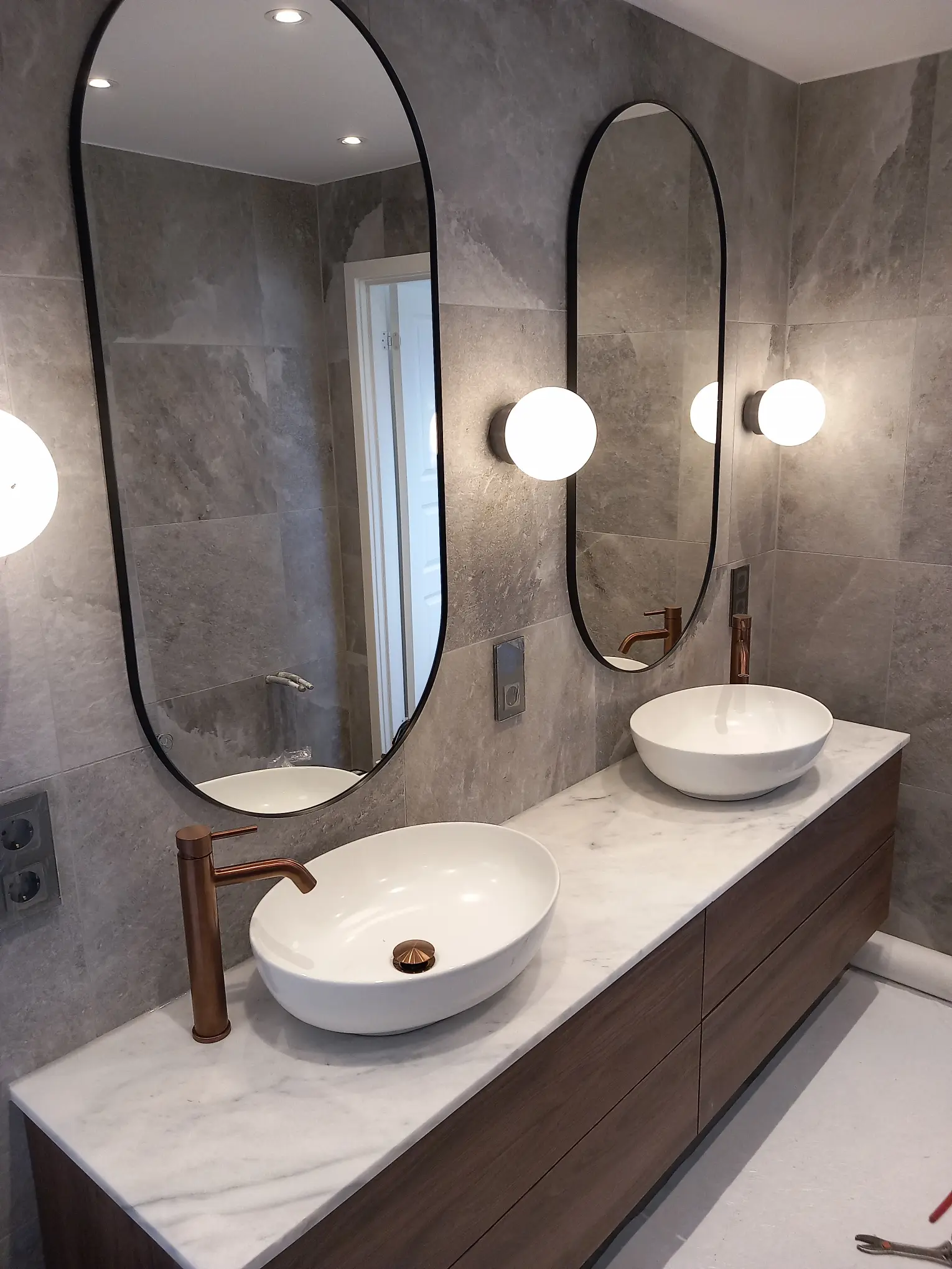 Badrumsrenovering med dubbla handfat, runda speglar och modern väggbelysning, perfekt för par.