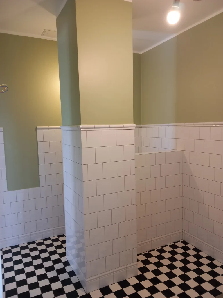 Detalj av badrumsrenovering, stilren övergång mellan vitt kakel och lugna gröna väggar, typisk för tidig funkis.